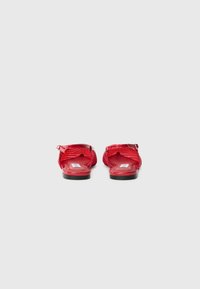 Sandales rouges avec une tige en mesh, un design à bout ouvert et une semelle noire, mettant en valeur un matériau texturé et des détails de sangle ajustable.