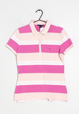 Vaaleanpunainen ja beige raidallinen lyhythihainen poolopaita, jossa neljä nappia, pieni logo rinnassa, roikkuu mustassa vaateripustimessa.