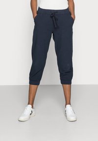 Pantalones recortados de color navy con cintura elástica y cordón, que cuentan con bolsillos laterales y puños acanalados, combinados con zapatillas blancas.
