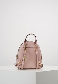 Růžový mini batoh z faux kůže se zlatými kovovými detaily, nastavitelné popruhy a malou horní rukojetí; zaoblený tvar s prošívanými detaily.