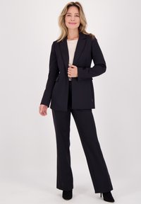 Zwarte op maat gemaakte blazer met een revers, slim fit, gecombineerd met bijpassende zwarte wijde broek en zwarte hakken.