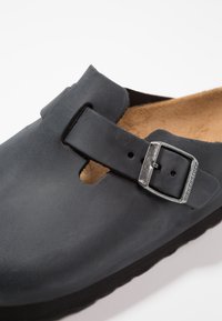 Chaussure noire en cuir à enfiler avec un bout rond, sangle ajustable avec une boucle en argent et une semelle en liège rembourrée.