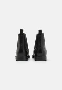 Black leather ankle boots with elastic side panels, pull tabs, and flat soles, featuring a smooth texture and minimalist design.