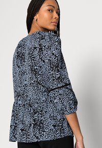 Blusa preta com padrão abstrato azul claro; apresenta mangas bufantes e estilo peplum, feita de um tecido leve e macio.
