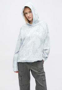 Világoskék kapucnis pulóver ágakat utánzó texturált mintával, elől zsebbel, bő szabással és zsinóros kapucnival.