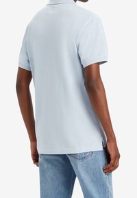 Ljusblå polo skjorta med klassisk krage, korta ärmar och sidokilar, tillverkad av mjukt tyg. Bakifrån syns ingen synlig branding.