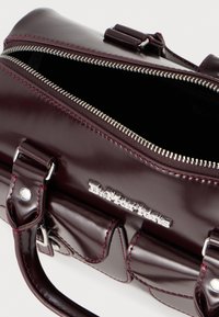 Burgundi patendinahk kott hõbedaste tõmblukkude ja riistadega. Omab kaht käepidet ja tikandite detaile, näidates poleeritud viimistlust.