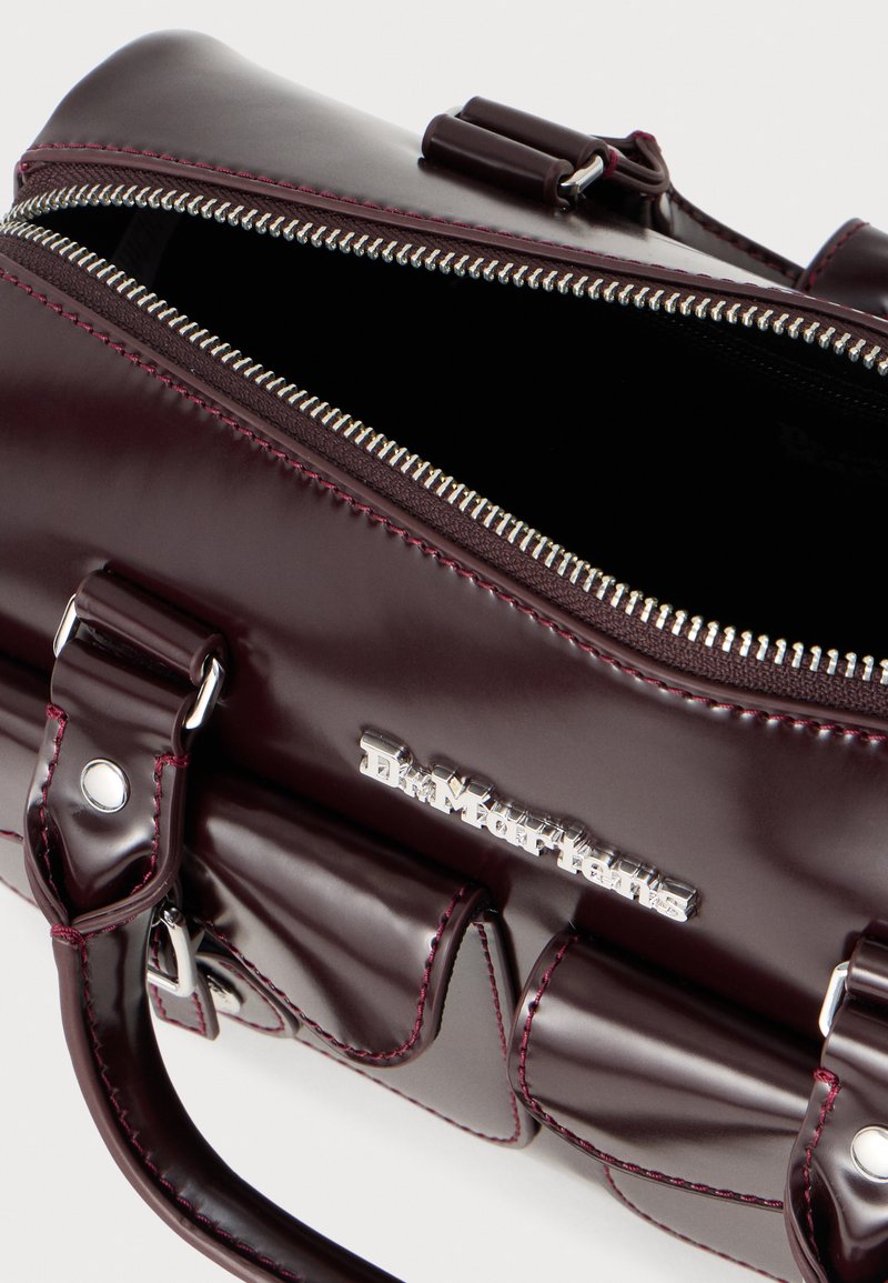 Borsa in pelle verniciata bordeaux con zip e hardware argentati. Presenta doppi manici e dettagli di cucitura, che mettono in risalto una finitura lucida.