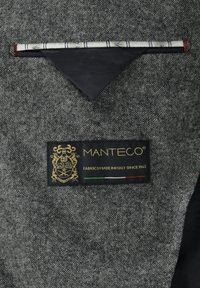 Gray textured fabric with a black label featuring gold text that reads "Manteco," along with a red and green accent and an emblem.