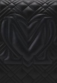 Svart läderhandväska med ett kviltat mönster och präglad logotypdesign. Texturen är slät med subtila sömmar.