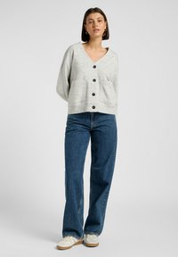 Ljust grå cardigan med v-ringning, knappfram, och två framfickor, ihop med blå vida jeans och vita sneakers.