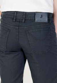 Pantaloni in cotone grigio scuro con cuciture a contrasto, dotati di due tasche posteriori e una etichetta in pelle con logo in vita.