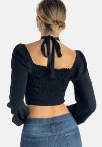 Sort cropped top med puffærmer, smocked tekstur, åben ryg med snørelukning og en tætsiddende silhuet. Stylet med blå jeans.