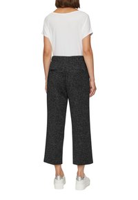 Pantalon large noir texturé à taille haute, associé à un t-shirt blanc uni et des baskets à plateforme argentées.