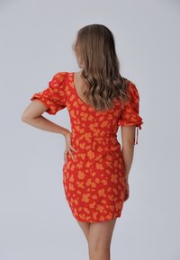 Röd klänning med korta puffärmar, öppen rygg och ett oranget blommönster, som sitter åt kroppen med en minilängd på fållen.