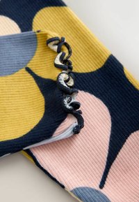 Tela de punto con textura acanalada, formas abstractas grandes multicolor y un detalle de borde negro con volantes en una sección doblada.