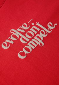 La tela roja presenta un gran texto de color crema que dice "evoluciona - no obligues". El material es algodón con una textura suave.