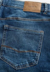 Denim jeans in een vervaagde blauwe kleur, met een enkele achterzak en een bruin leren label met de tekst "DENIM SUPPLY Co." op de tailleband.