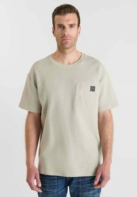 Lichtbeige textuur T-shirt met een ronde halslijn, korte mouwen en een borstzak met een zwart labeldetail.