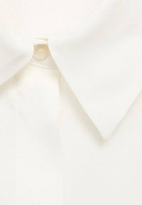 Gros plan d'un col de chemise blanc avec un bouton visible sous les pointes du col.