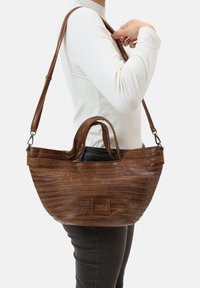 Sac à main en cuir marron avec une forme arrondie, texture gaufrée horizontale, deux poignées et une bandoulière réglable. Étiquette de la marque visible.