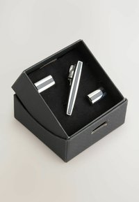 Srebrny zestaw spinki do krawata i mankietów w czarnym pudełku. Spinka do krawata ma elegancki design z prostymi liniami, a spinki do mankietów są prostokątne.