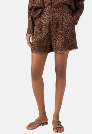 Leopardprintede shorts med høj talje og rå kant, kombineret med matchende langærmet top, båret af person iført flade sandaler med stropper.