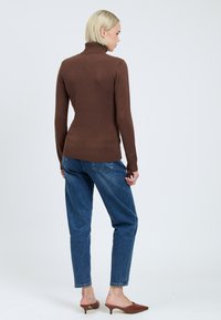 Brauner Rollkragenpullover mit langen Ärmeln, tailliertem Schnitt und gerippter Textur, kombiniert mit blauen schmalen Jeans und braunen offenen Mules.