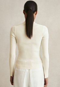 Krémový žebrovaný dlouhý rukáv top s fitting siluetou, s bočními rozparky na lemu a vysokým výstřihem, vyrobený z texturované látky.