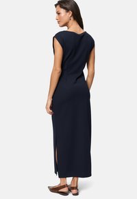 Navyblaues Maxikleid mit kurzen Ärmeln, hat eine gerade Silhouette und seitliche Schlitze. Getragen mit braunen, flachen Slingback-Schuhen.
