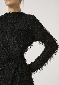 Schwarzer strukturierter Pullover mit lockeren Fasern an den Kanten und Ärmeln, hochgeschlossener Ausschnitt und oversized Design.