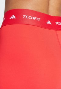 Røde Techfit træningsshorts med en bred elastisk talje, der har hvid branding. Materialet er glat og tætsiddende, designet til komfort.