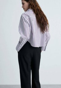Bluză stripedă albă cu dungi violet, cu o croială lejeră și o tiv curved. Asortată cu pantaloni negri, largi.