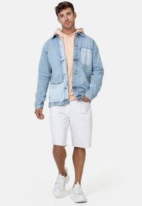 Světle modrá džínsová košile na knoflíky s náprsní kapsou, přes níž je položený světlý růžový hoodie, doplněné bílými šortkami a teniskami.