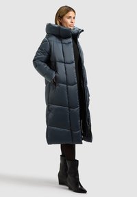 Pikk puffer-mantel tumesinisest materjalist, tikitud mustriga, suure kapuutsi ja kahe küljetaskuga. Omaduseks on sujuv, sile tekstuur ja tõmblukud.