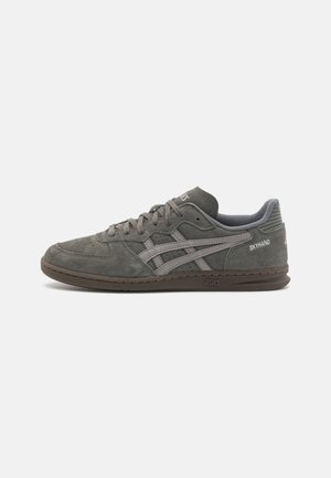 Grå lavtop Asics ruskindssneaker med snørebånd foran, perforerede sider og "Skyhand" branding på hælkappen.
