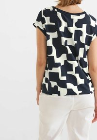 Mörkblå kortärmad topp med ett vitt abstrakt mönster. Mjuk tyg med avslappnad passform, rund halsringning och sänkta axlar.