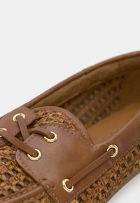 Mocassin en cuir marron et tissé avec des œillets dorés et des lacets en cuir assortis, affichant des coutures détaillées et une doublure intérieure douce.