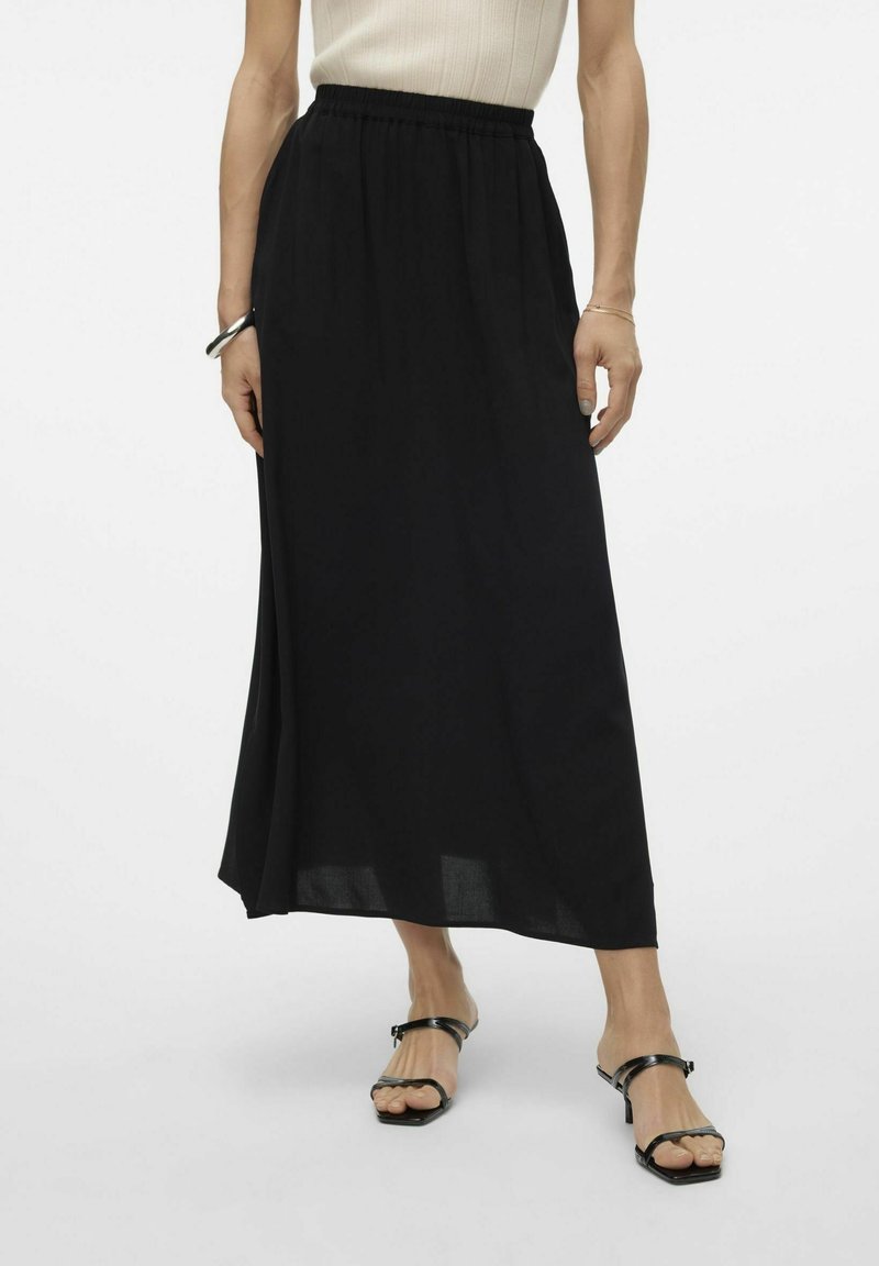 Jupe maxi noire avec taille élastique et tissu doux ; présente un design fluide qui arrive jusqu'aux chevilles. Associée à des sandales noires.