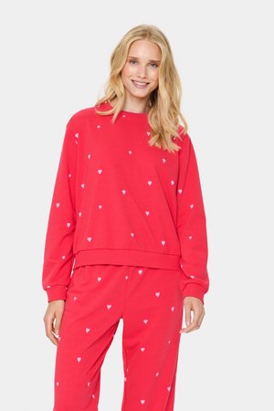 Set de pulover și pantaloni roșu dintr-un material moale, având un model repetitiv cu inimioare mici albe. Croială lejeră, cu manșete și talie ribbate.