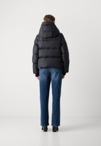 Doudoune noire avec capuche et design matelassé, associée à un jean en denim bleu à jambe droite et des bottes noires épaisses.