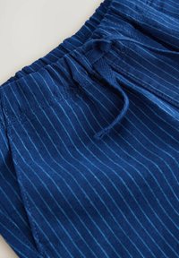 Tissu rayé bleu avec une taille élastique et un cordon de serrage. La texture semble lisse avec de fines lignes verticales.