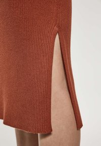 Abito a maglia a coste color ruggine con spacchi laterali, caratterizzato da una consistenza morbida e orlo dritto. Il design si concentra su una silhouette slim.