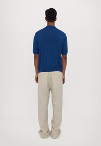 Niebieska koszulka polo z krótkim rękawem o teksturowanym wykończeniu, zestawiona z jasnobeżowymi spodniami o szerokiej nogawce, widok od tyłu.