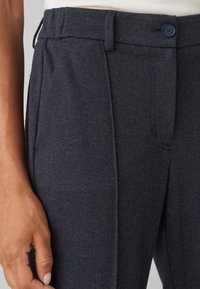 Navy herringbone byxor med veckad design, sidofickor och knäppning i midjan. Slät textur med skräddarsydd passform.