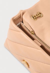Bolsa de mão em pele pêssego com um design matelassé, apresentando ferragens douradas, um bolso com fecho e um detalhe em botão. Textura suave em toda a superfície.
