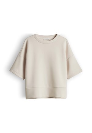 Sweat-shirt beige oversize à manches courtes, épaules tombantes et encolure ronde, présenté sur un fond blanc.