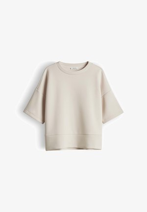 Sweat-shirt beige oversize à manches courtes, épaules tombantes et encolure ronde, présenté sur un fond blanc.