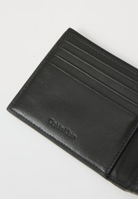 Černá kožená peněženka s vícero přihrádkami na karty, hladkým povrchem a vyrytým logem. Kompaktní design s pečlivým prošitím.