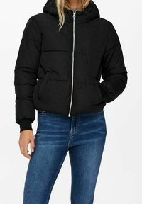 Sort dunjakke med hætte, frontlynlås og to sidelommer. Har et quiltet design og elastiske manchetter, båret over blå jeans.